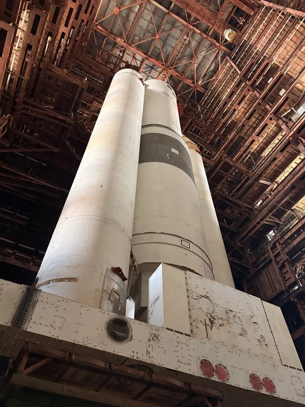 A huge white rocket stage standing in the hangar, seen from below.