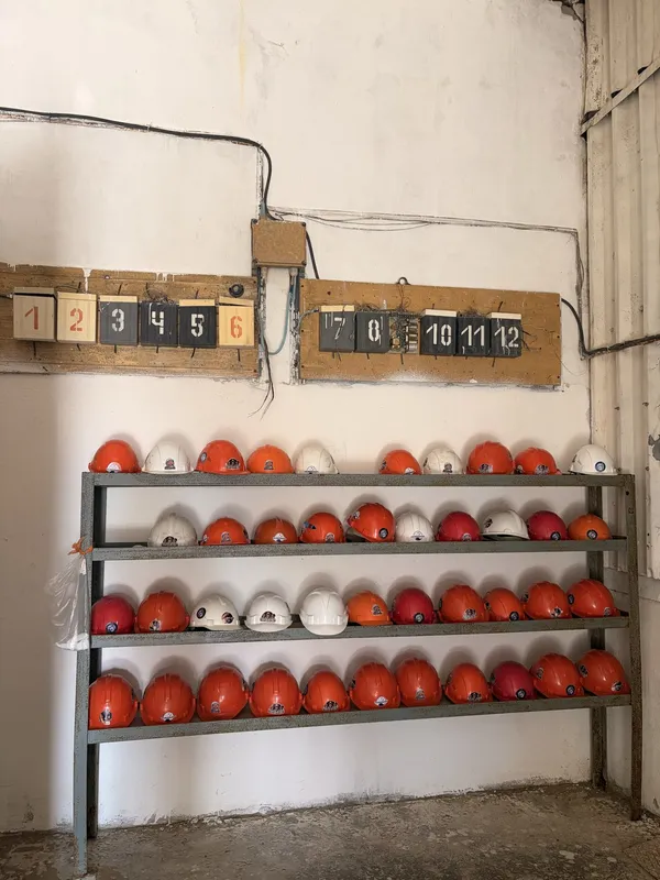 Rows of red and white hard hats on a rack under a numbered board.