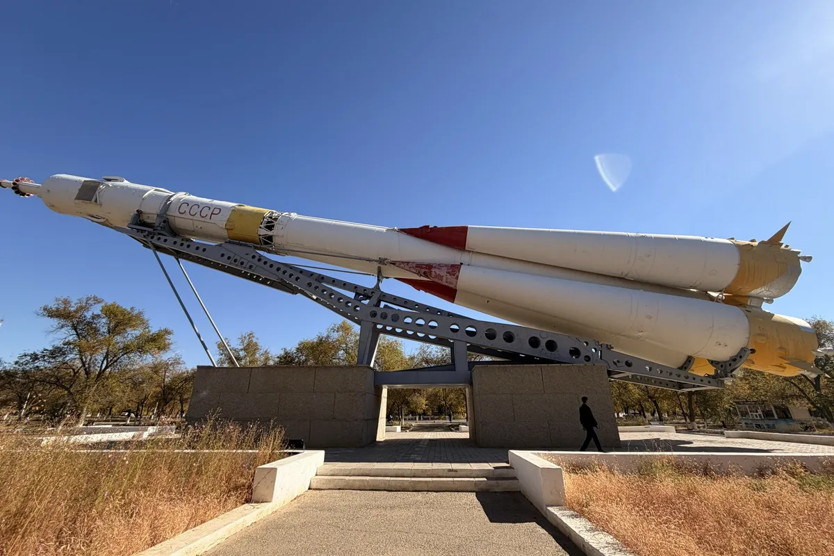 A full-size rocket monument, mounted at an angle on a plinth, against a blue sky.