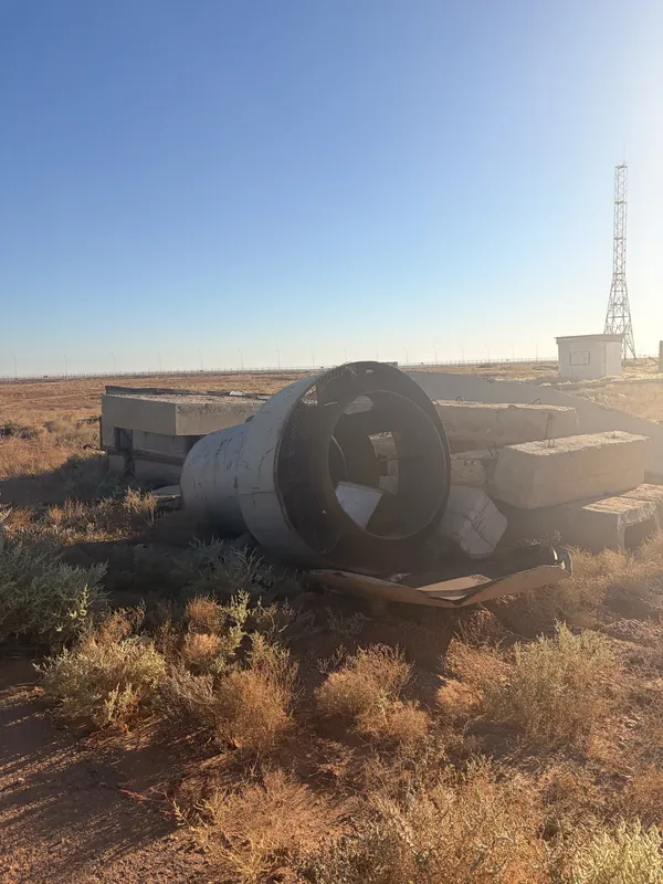 A rusted cylindrical section of rocket hardware lying in the steppe scrub.