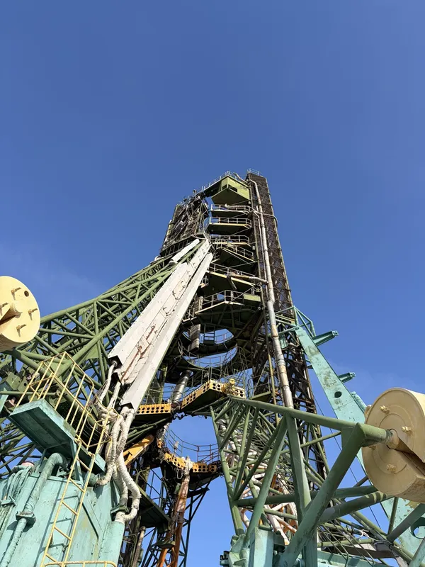 Looking up at the tall green service structure of the launch pad against a blue sky.