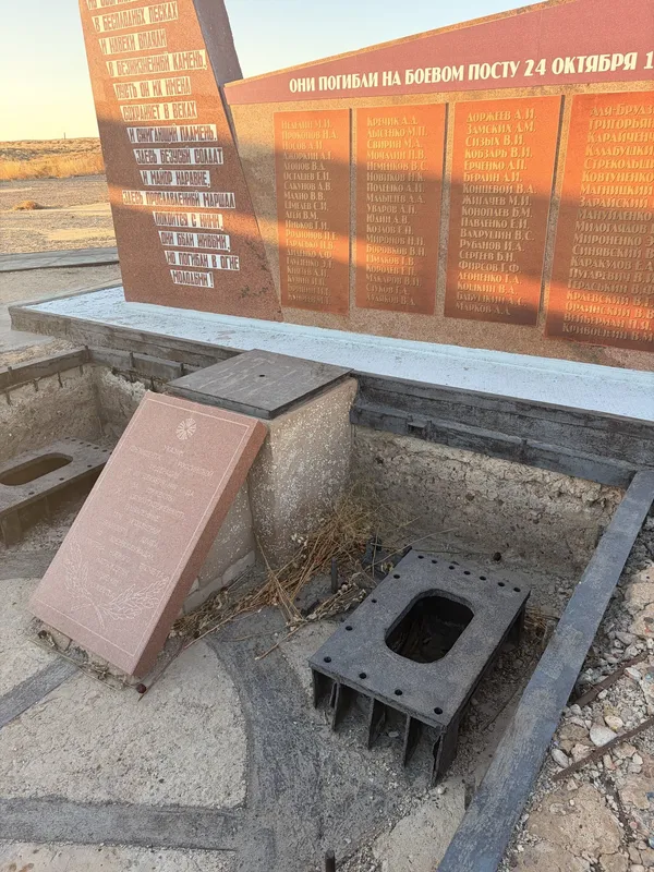 A red memorial wall listing names, with a small plaque and a grate in the ground in front.