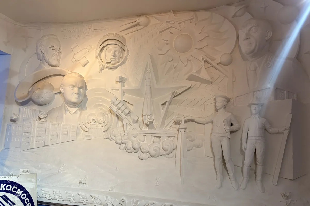 A white plaster relief of cosmonauts, rockets and a sun, lit from the side.