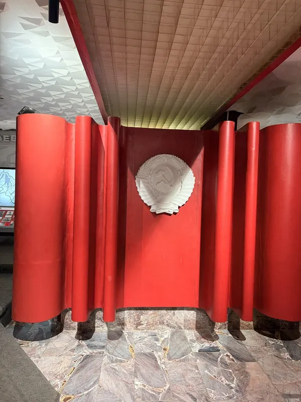A red sculptural entrance with vertical fins and a round emblem.