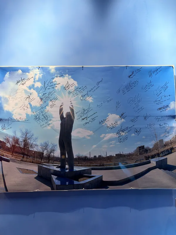 A large photograph of a figure with raised arms against the sky, covered in signatures.