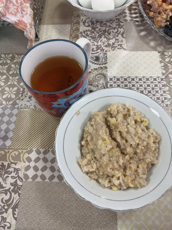 A bowl of porridge and a mug of tea on a patterned tablecloth.