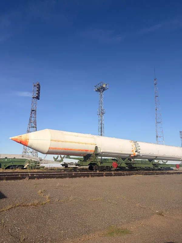 A rocket lying on a rail transporter at a pad, floodlight masts behind.