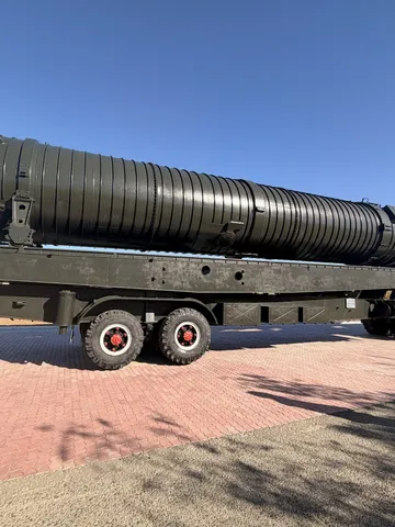 A long missile container on a wheeled trailer, a visitor walking past.