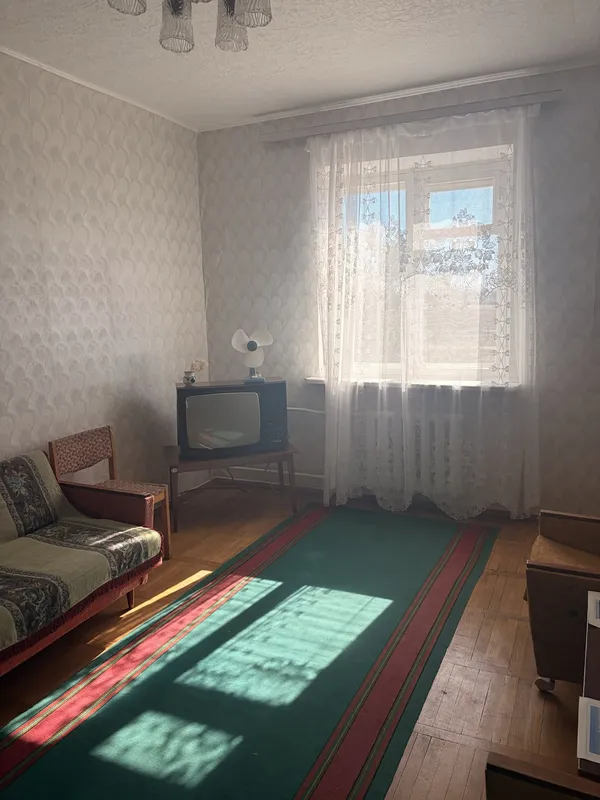 A small room with patterned wallpaper, a sofa, an old television and sun through lace curtains.