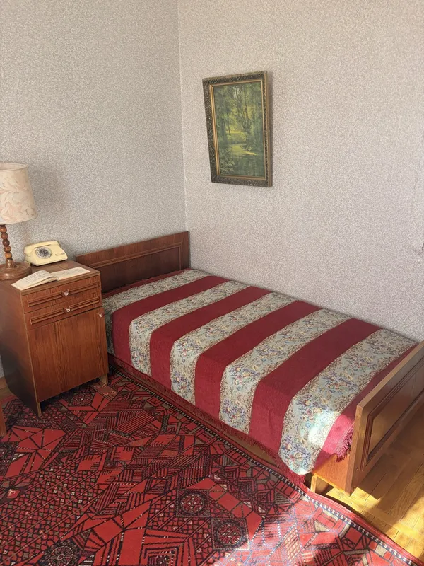 A single bed with a red and white striped cover, a bedside cabinet and a framed painting.